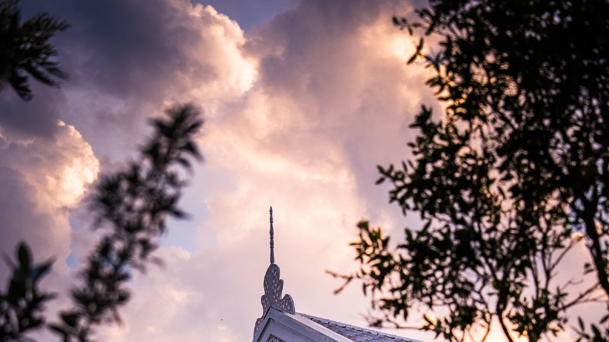 The white gabled roofline of WIROON, its carved monogram catching the light, framed by garden trees against an evening sky