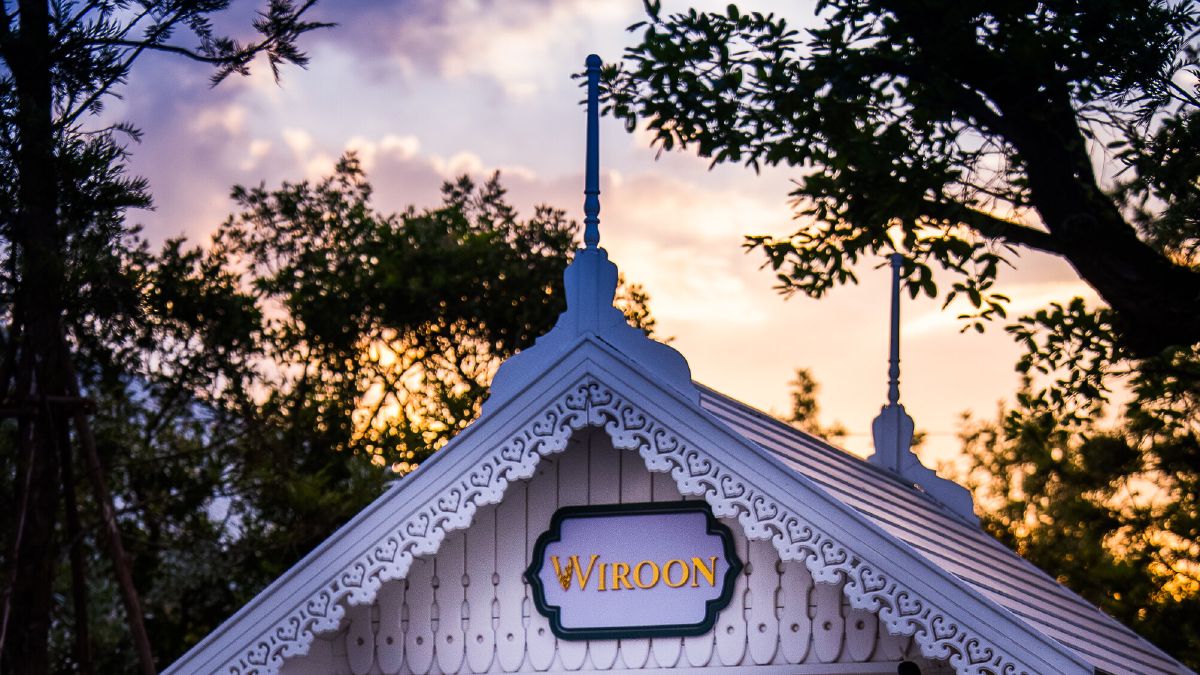 The white entrance gate of WIROON lit at dusk, its doors open onto a stone path leading into the gardens