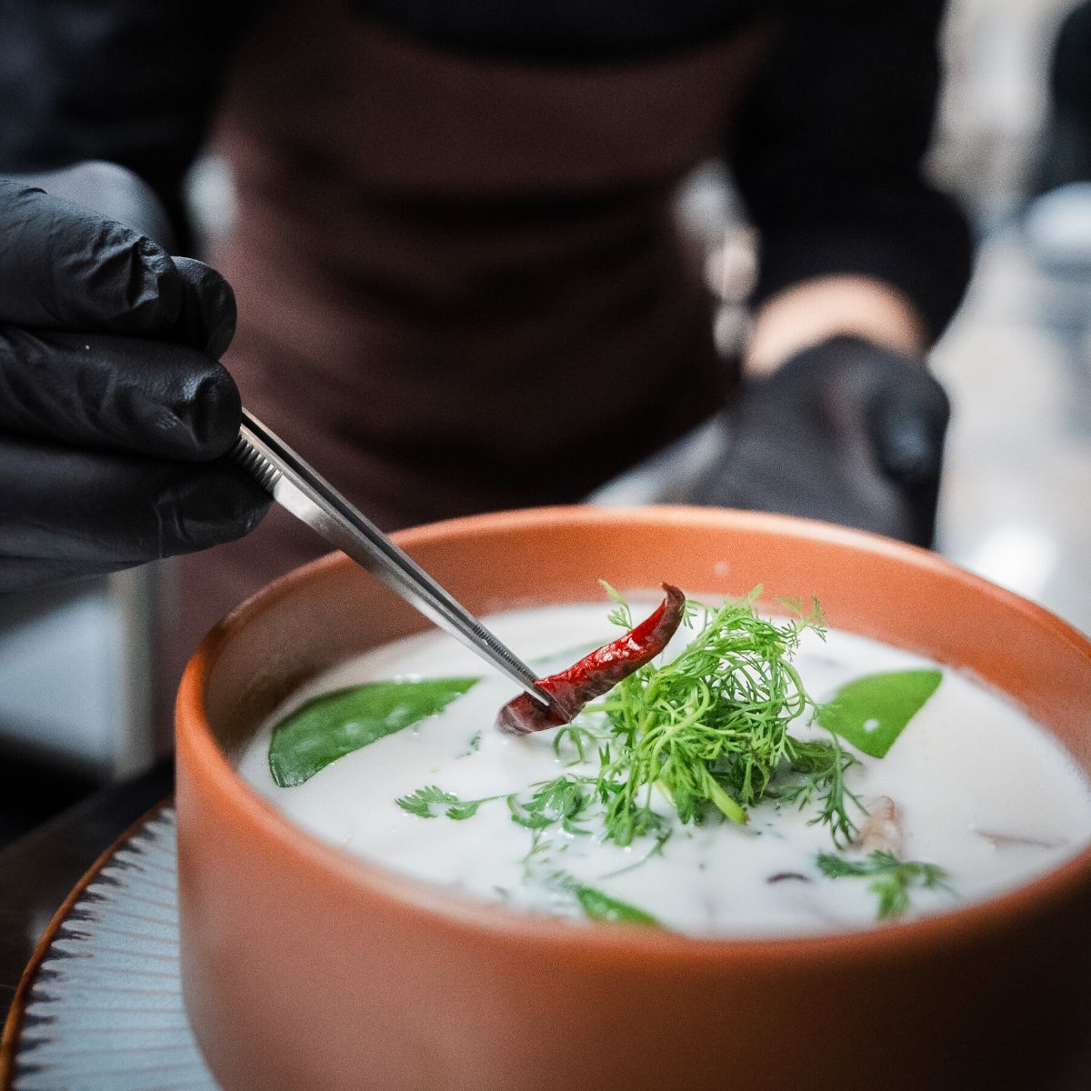 A chef plating food into an earthenware bowl in the WIROON kitchen