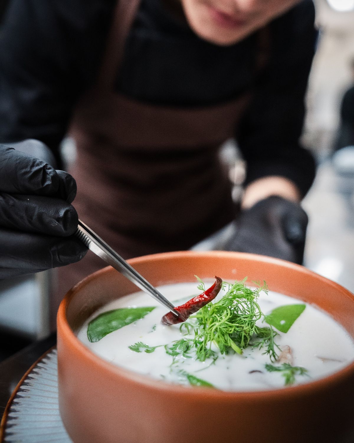 A chef plating food into an earthenware bowl in the WIROON kitchen